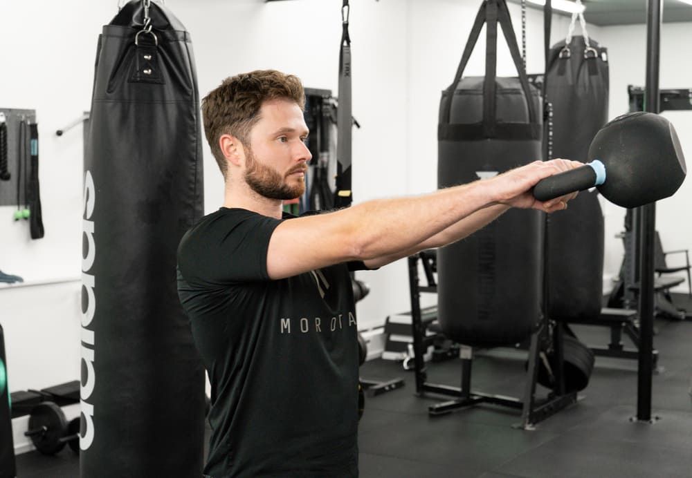 Mann beim Training mit einer Kettlebell im Fitnessstudio von Bootcamp Essen, konzentrierter Blick, umgeben von Boxsäcken und Trainingsgeräten.
