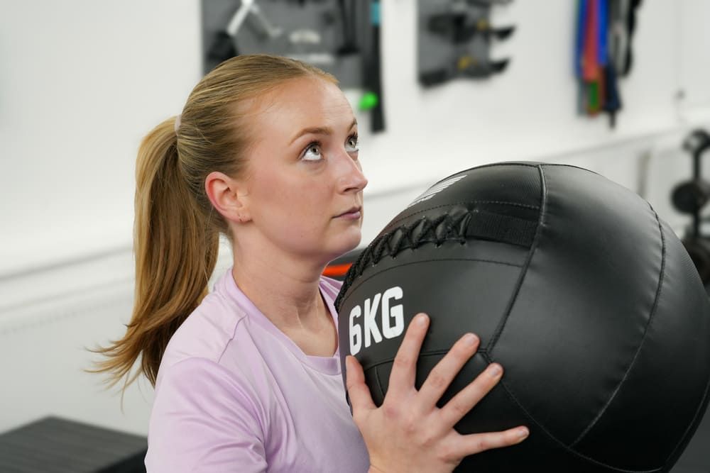 Junge Frau im Fitnessstudio hält einen 6-Kilogramm-Medizinball vor der Brust und schaut konzentriert nach oben – Training im Bootcamp Essen.