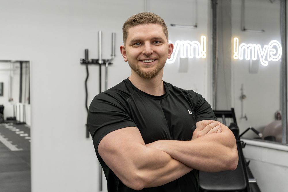 Personal Trainer Pascal Nies in Sportkleidung steht mit verschränkten Armen in einem modernen Fitnessstudio in Essen und lächelt selbstbewusst in die Kamera